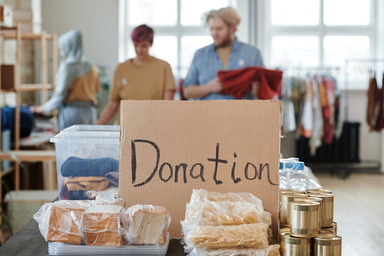 about-us Volunteers sort clothes and food in a donation center. Cardboard sign reads 'Donation.'
